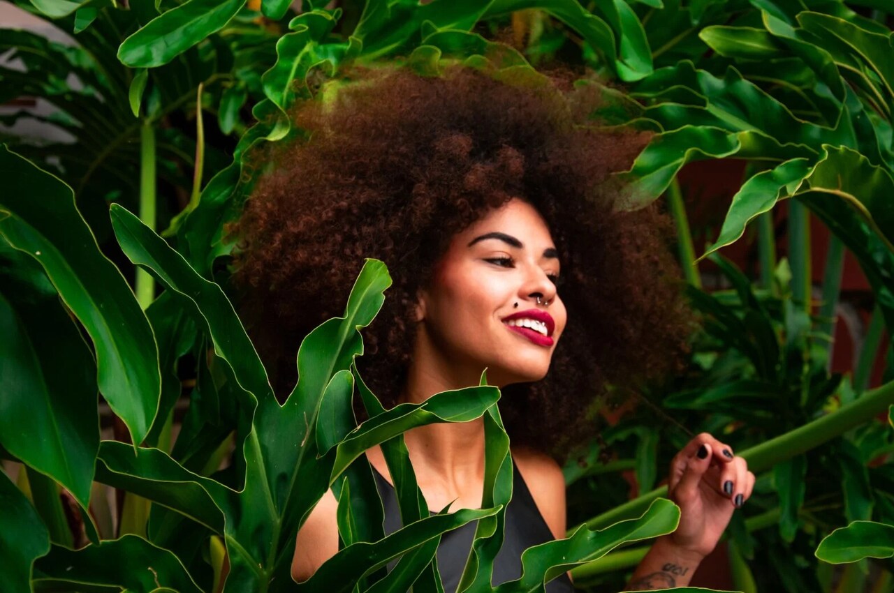 Model with natural curly hair among tropical leaves, Cantu Beauty campaign image